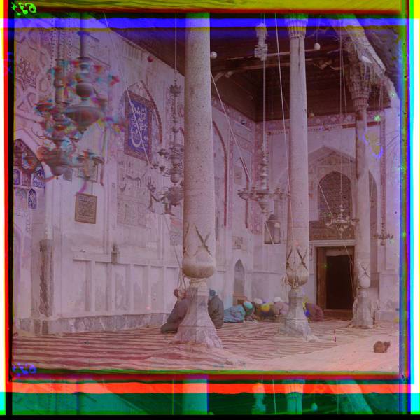 group_of_men_seated_on_rugs_praying_under_hanging_candalabras_inside_a_mosque.jpg