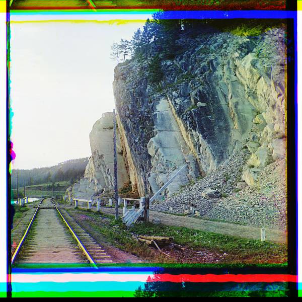 railroad_tracks_and_utility_poles_along_a_waterway_and_cliff_with_road_crossing.jpg